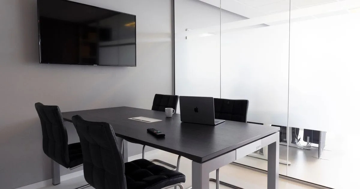 A modern meeting room with a conference table, laptop and display